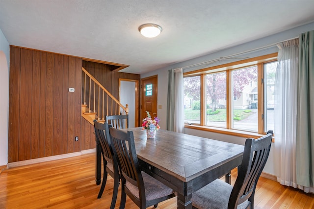 dining space with baseboards, stairs, light wood-style floors, and wood walls