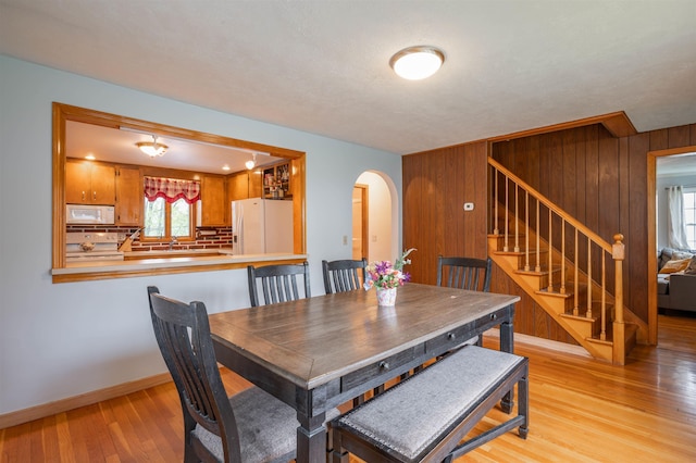 dining space with arched walkways, stairs, light wood-style floors, wooden walls, and baseboards