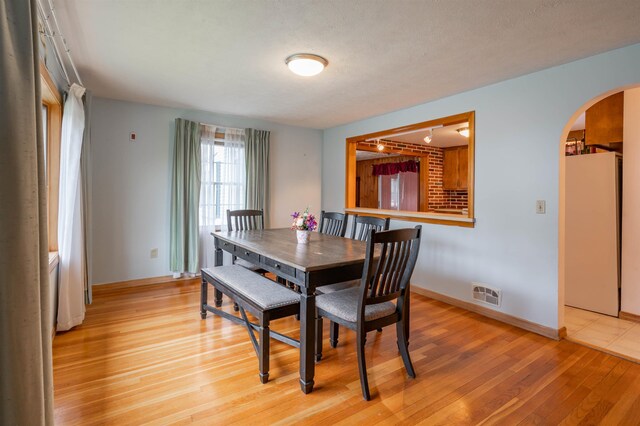 dining area with arched walkways, light wood-type flooring, and baseboards