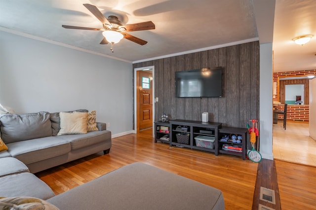 living area featuring ceiling fan, wood finished floors, ornamental molding, wood walls, and baseboards