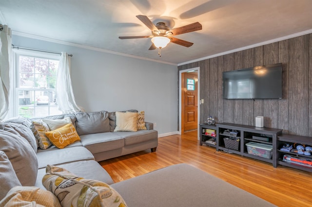 living room with wooden walls, ceiling fan, ornamental molding, wood finished floors, and baseboards