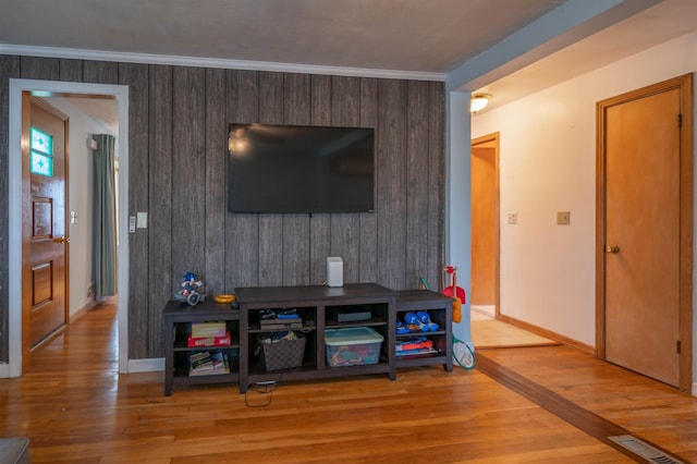 living room with light wood-style flooring, baseboards, ornamental molding, and wooden walls