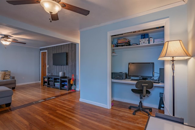 office space with a ceiling fan, wood finished floors, ornamental molding, baseboards, and an accent wall