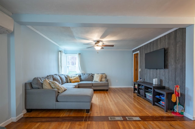 living area featuring a wall unit AC, wood finished floors, baseboards, crown molding, and a ceiling fan