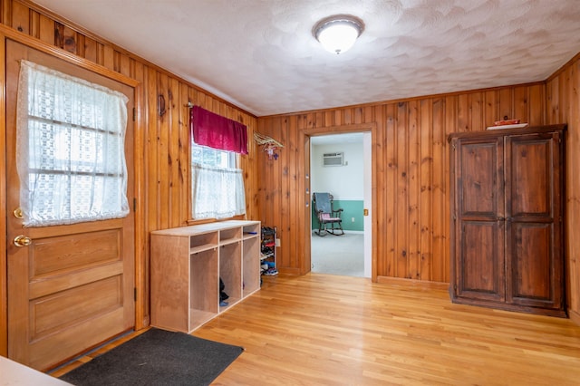 foyer with wood walls, a wall unit AC, light wood finished floors, and a textured ceiling