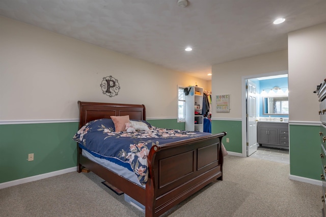 bedroom with light colored carpet, recessed lighting, baseboards, ensuite bath, and a walk in closet