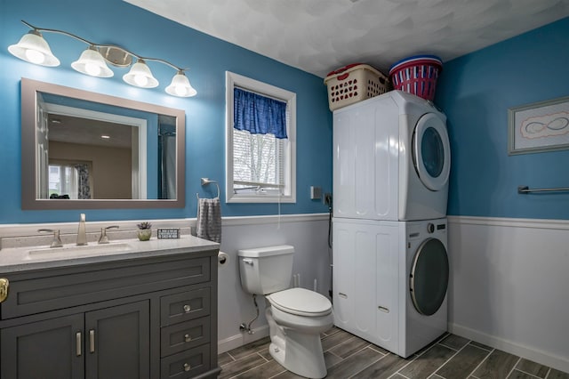 bathroom featuring stacked washing machine and dryer, wood tiled floors, toilet, vanity, and baseboards