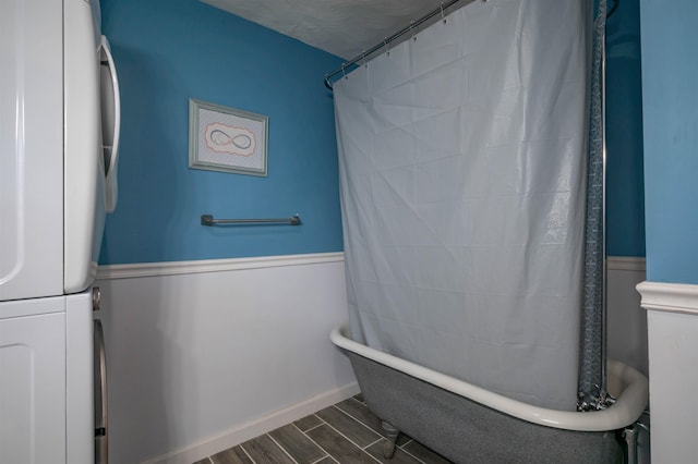 bathroom with stacked washer and clothes dryer, a tub, wood finished floors, and a shower with curtain