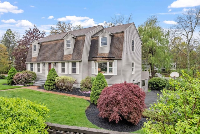 dutch colonial with a gambrel roof, roof with shingles, and a front lawn