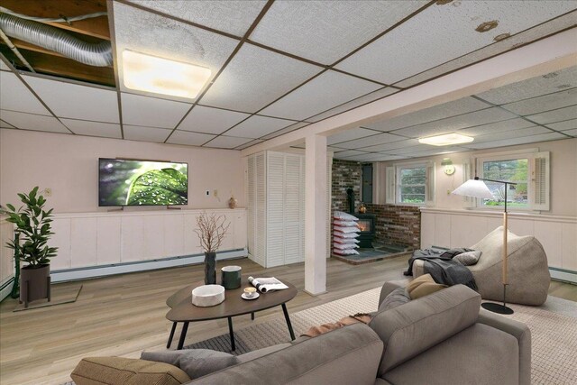 living room with a drop ceiling, a baseboard heating unit, wood finished floors, and wainscoting