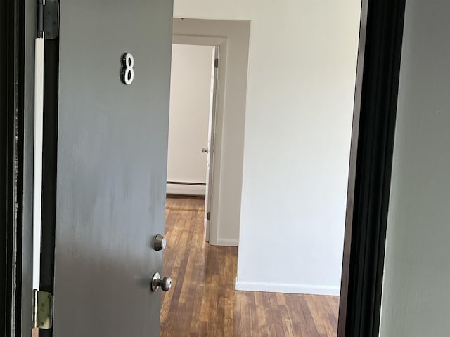 hallway featuring a baseboard radiator, wood finished floors, and baseboards