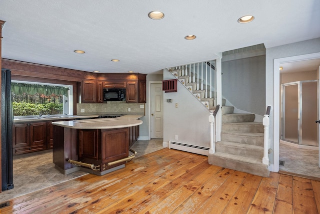 kitchen with black microwave, a baseboard radiator, light wood-type flooring, light countertops, and recessed lighting