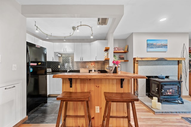 kitchen featuring freestanding refrigerator, a wood stove, white cabinets, a sink, and a kitchen bar