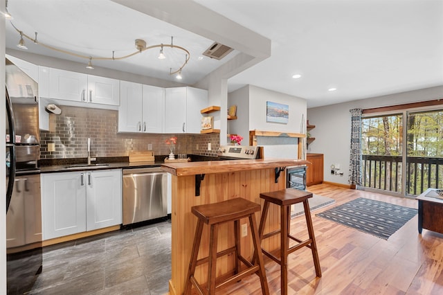 kitchen with appliances with stainless steel finishes, a sink, open shelves, a kitchen bar, and decorative backsplash