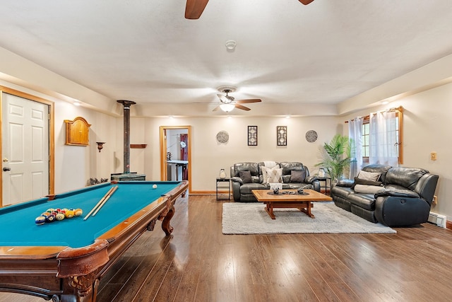 game room with a ceiling fan, a wood stove, a baseboard radiator, and wood finished floors