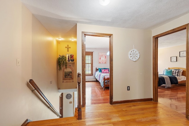 corridor with an upstairs landing, light wood-type flooring, a textured ceiling, and baseboards