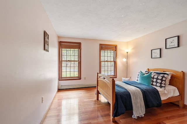 bedroom featuring a baseboard heating unit, light wood finished floors, and baseboards