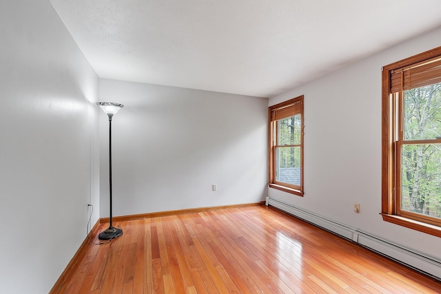 unfurnished room featuring a baseboard heating unit, light wood finished floors, and baseboards