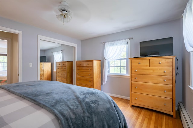 bedroom with baseboard heating, light wood-style flooring, a closet, baseboards, and ceiling fan