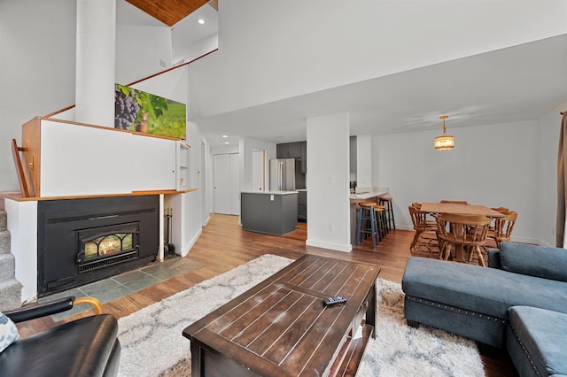 living room featuring wood finished floors, baseboards, a fireplace with flush hearth, and a towering ceiling