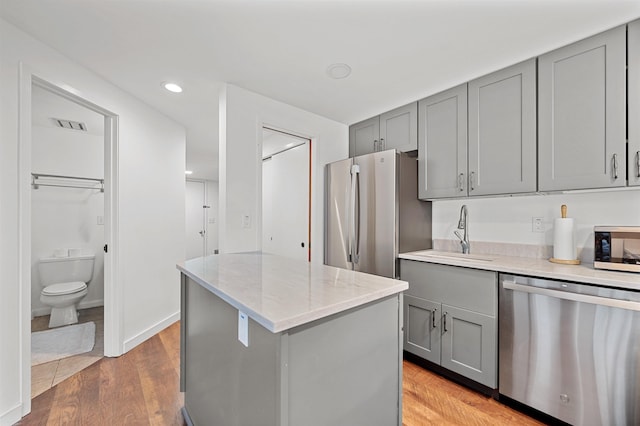 kitchen with stainless steel appliances, gray cabinets, a sink, a center island, and light stone counters