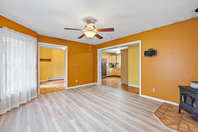 56 Call Rd, Webster, NH 03303 - unfurnished living room featuring baseboard heating, a wood stove, a ceiling fan, light wood-style floors, and baseboards