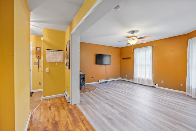 56 Call Rd, Webster, NH 03303 - unfurnished living room featuring light wood finished floors, a ceiling fan, baseboards, a wood stove, and a baseboard radiator