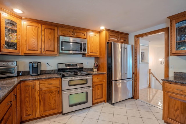 1 Alpine Rd, Windham, NH 03087 - kitchen with appliances with stainless steel finishes, brown cabinetry, glass insert cabinets, dark stone counters, and light tile patterned floors