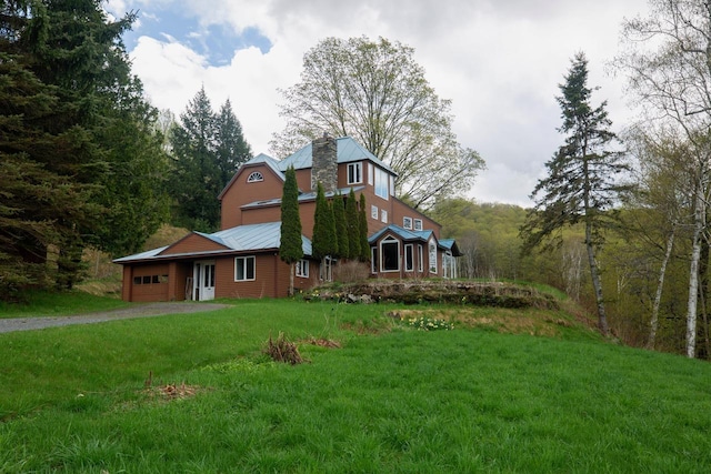 view of front facade with an attached garage, dirt driveway, a chimney, a front yard, and metal roof
