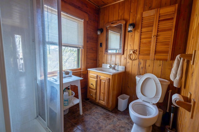 bathroom featuring wooden walls, a shower stall, toilet, vanity, and tile patterned flooring