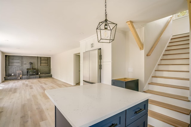 kitchen featuring a wood stove, fridge, light wood-style floors, white cabinetry, and pendant lighting