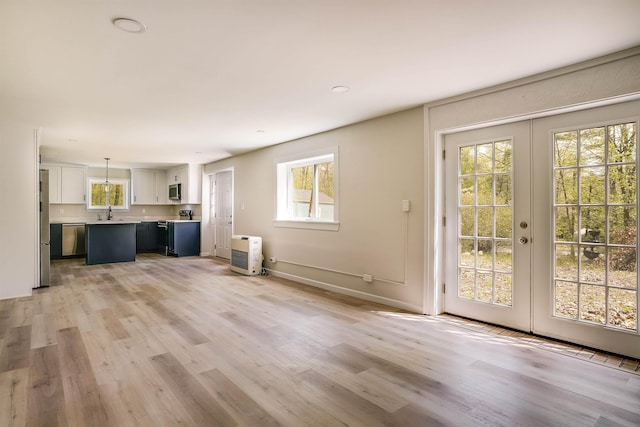 unfurnished living room with plenty of natural light, light wood-style floors, and french doors