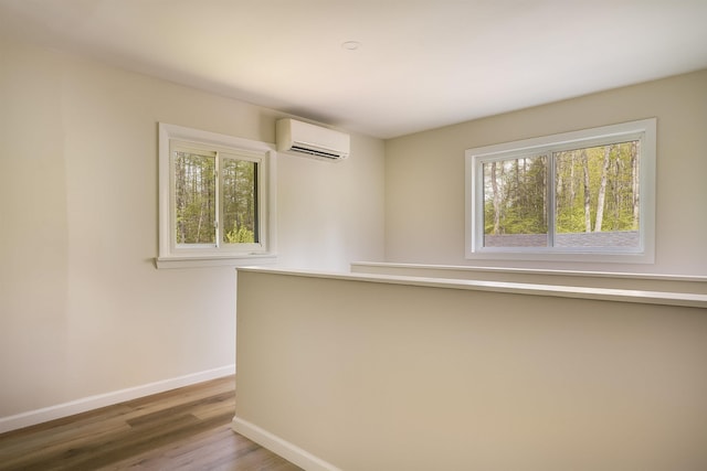 empty room with a wall unit AC, healthy amount of natural light, baseboards, and wood finished floors