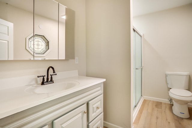 bathroom featuring wood finished floors, toilet, a shower stall, vanity, and baseboards
