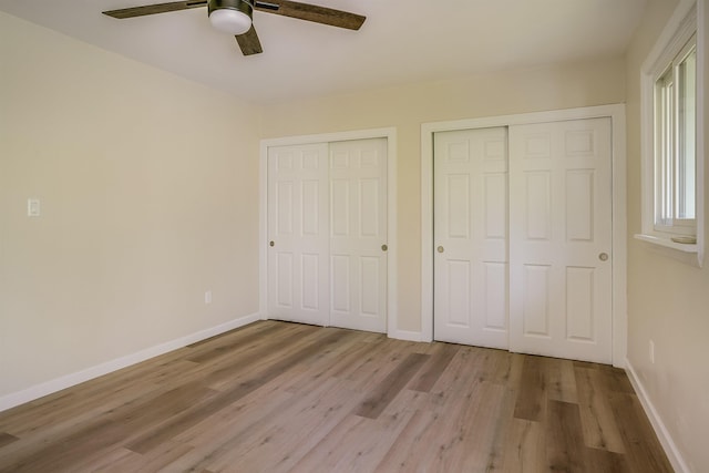 unfurnished bedroom with multiple closets, wood finished floors, baseboards, and a ceiling fan