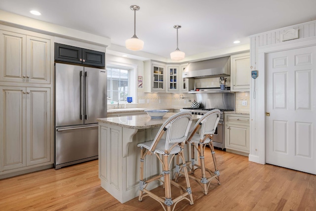 150 Webhannet Dr, Wells, ME 04090 - kitchen featuring high end appliances, wall chimney range hood, light wood-style flooring, tasteful backsplash, and glass insert cabinets
