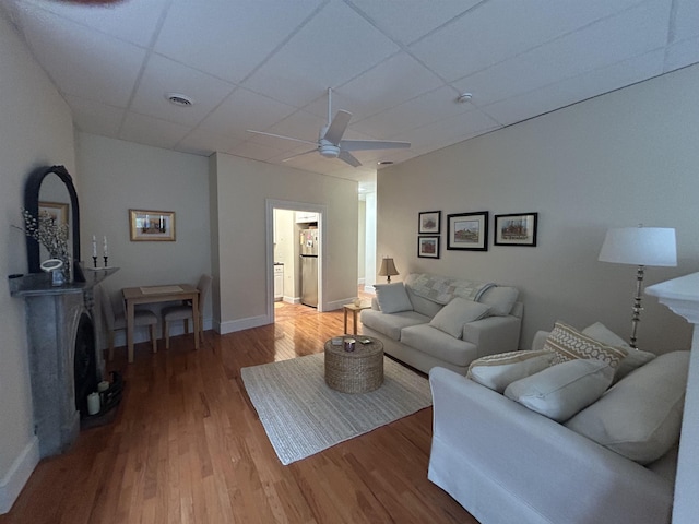 living area with a drop ceiling, baseboards, light wood-type flooring, and ceiling fan