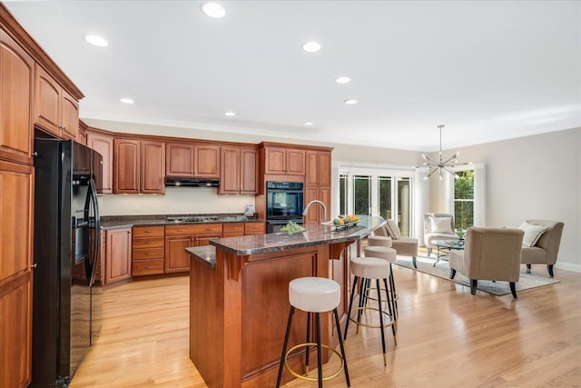 371 Tibbetts Hill Rd, Goffstown, NH 03045 - kitchen with black appliances, a breakfast bar, under cabinet range hood, brown cabinetry, and a kitchen island with sink