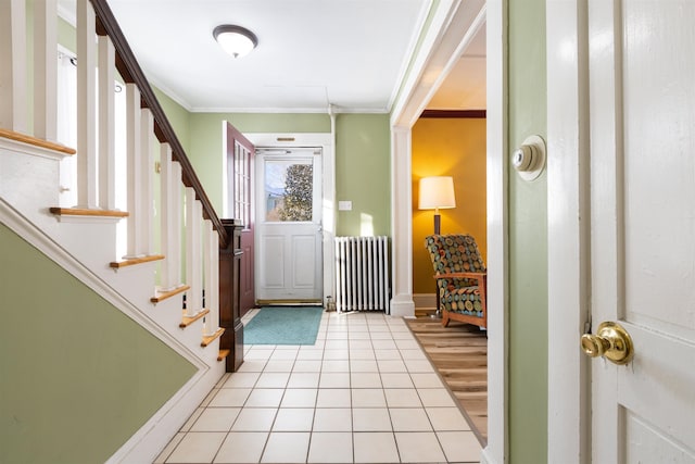 foyer entrance featuring radiator heating unit, ornamental molding, light tile patterned flooring, stairway, and baseboards