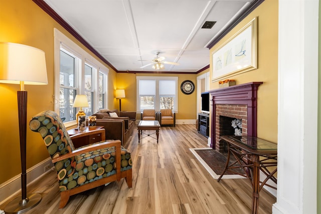 sitting room with light wood-style flooring, a brick fireplace, baseboards, crown molding, and ceiling fan