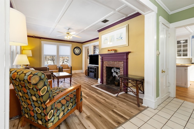 living area featuring a fireplace, ornamental molding, ceiling fan, light wood-style flooring, and baseboards