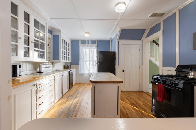 kitchen featuring black gas stove, freestanding refrigerator, a center island, light wood-style floors, and light countertops