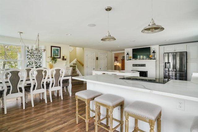 kitchen with stainless steel fridge, dark wood-style floors, hanging light fixtures, white cabinets, and a breakfast bar area