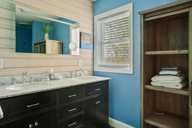 full bathroom with healthy amount of natural light, double vanity, wooden walls, and baseboards