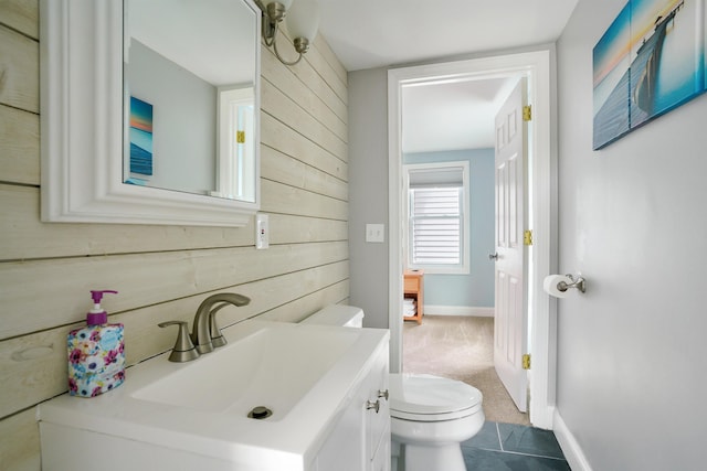 bathroom with toilet, vanity, wood walls, and baseboards
