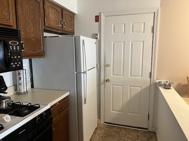 kitchen with range with gas stovetop, black microwave, light countertops, and freestanding refrigerator