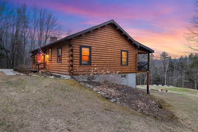 property exterior at dusk with a chimney, log siding, and a lawn