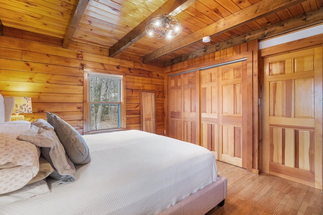 bedroom featuring beam ceiling, light wood finished floors, wooden walls, a closet, and wood ceiling