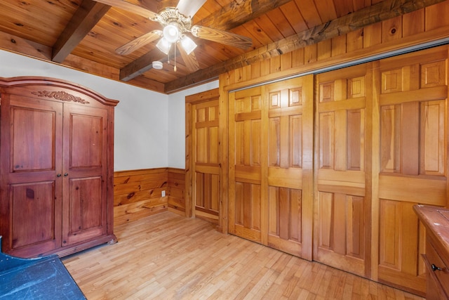 unfurnished bedroom featuring wooden ceiling, beamed ceiling, light wood finished floors, wood walls, and a wainscoted wall