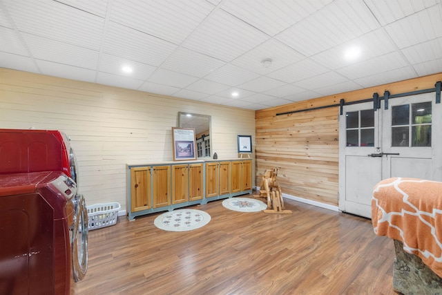 sitting room featuring light wood-type flooring, wooden walls, a barn door, baseboards, and a paneled ceiling